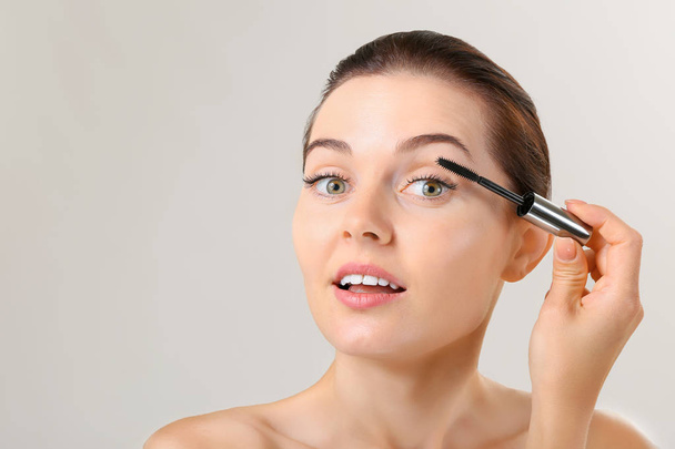 Beautiful young woman with eyelash extensions applying mascara against grey background - Φωτογραφία, εικόνα