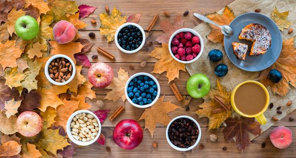 Szezonális őszi háttér. Juharlevél és torta, bogyók, mazsola, alma, gyümölcsök, kávé és diófélék fából készült háttérrel. - Fotó, kép
