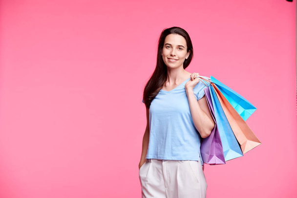 Young pretty shopaholic with shoppng bags standing on pink background in isolation - Photo, Image