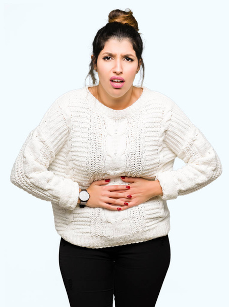 Young beautiful woman wearing winter sweater with hand on stomach because indigestion, painful illness feeling unwell. Ache concept. - Photo, Image