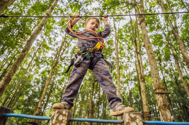 Um rapazinho num parque de cordas. Recreação física ativa da criança ao ar livre no parque. Treinamento para crianças
 - Foto, Imagem