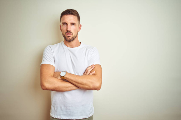 Young handsome man wearing casual white t-shirt over isolated background skeptic and nervous, disapproving expression on face with crossed arms. Negative person. - Foto, Bild