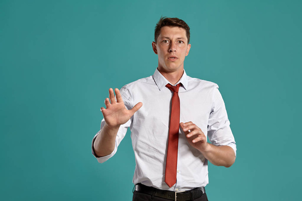 Молодой человек в классической белой рубашке и красном галстуке позирует на синем фоне
. - Фото, изображение