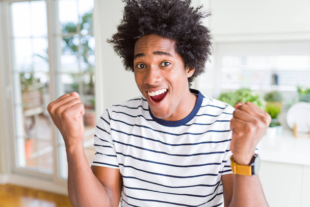 African American man dragen strepen t-shirt vieren verrast en verbaasd voor succes met armen verheven en open ogen. Winnaar concept. - Foto, afbeelding