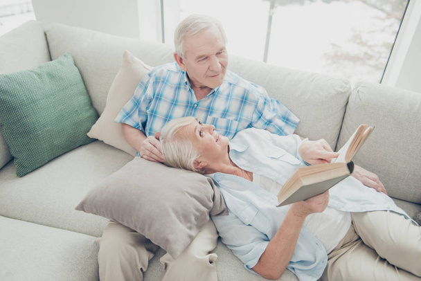 Portrait of her she his he two nice attractive cheerful cheery focused spouses sitting lying on divan reading new interesting book in light white interior living-room indoors - Photo, Image