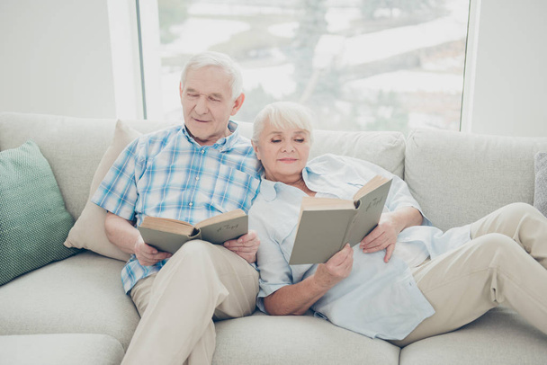 Portrait of her she his he two nice attractive focused concentrated peaceful calm spouses sitting on divan reading new interesting book in light white interior living-room indoors - Foto, afbeelding