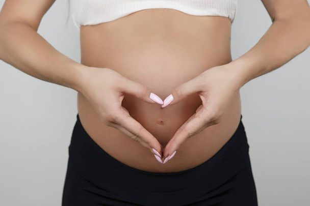 pregnant woman making heart sign with her hands on her naked pregnant belly isolated white background - Foto, imagen