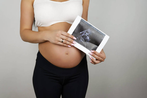 pregnant woman holding ultrasound picture of her baby on isolated white background - Foto, Imagem