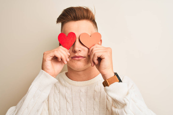 Young handsome romantic man holding paper hearts standing over isolated white background with a confident expression on smart face thinking serious - Fotoğraf, Görsel