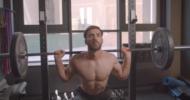 Closeup portrait of adult attractive caucasian man lifting weights making squats in the gym indoors - Video