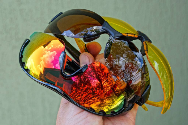 ręka posiada zestaw trzech kolorowych okularów przeciwsłonecznych na szarym tle - Zdjęcie, obraz