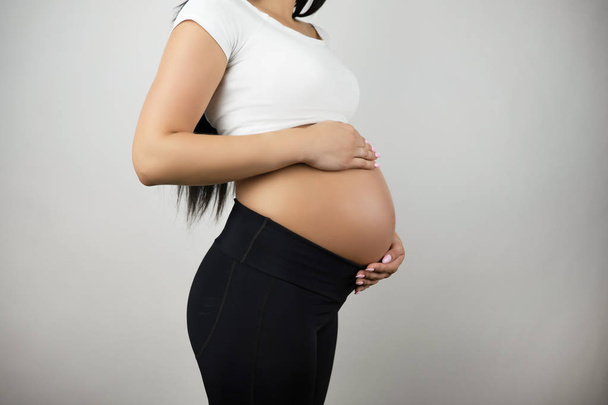 brunette young woman holding her pregnant naked belly on isolated white background - Valokuva, kuva