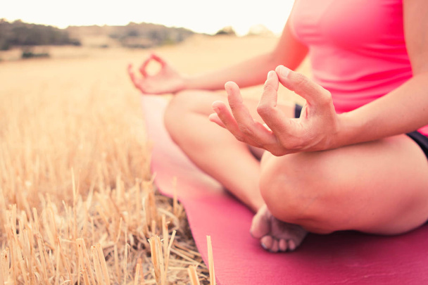 Cerca de las manos de una joven con ropa deportiva meditando y haciendo yoga pacíficamente en un campo abierto
 - Foto, Imagen