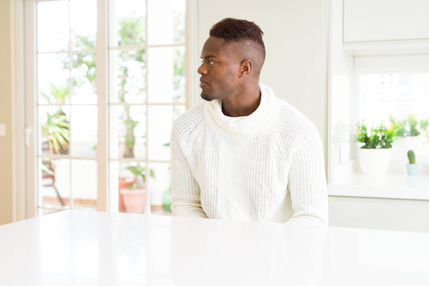 schöner afrikanisch-amerikanischer Mann auf weißem Tisch mit Blick zur Seite, entspannte Profil-Pose mit natürlichem Gesicht mit selbstbewusstem Lächeln. - Foto, Bild