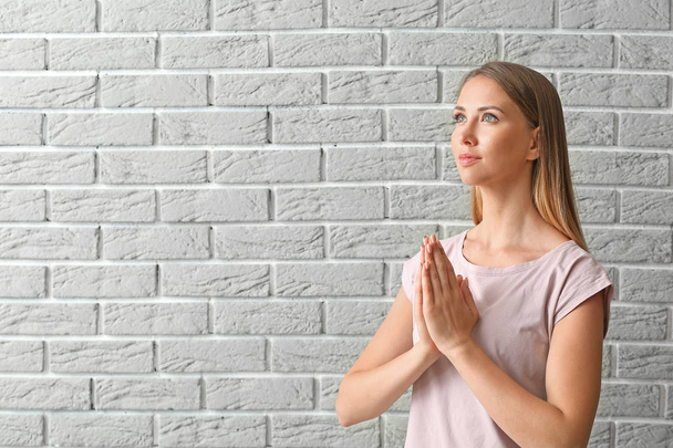 Religieuze jonge vrouw bidden tegen bakstenen muur - Foto, afbeelding