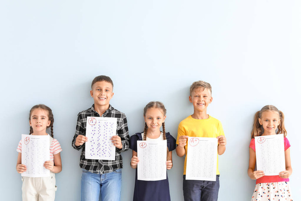 Bambini con fogli di risposta per test scolastici su sfondo di colore chiaro
 - Foto, immagini