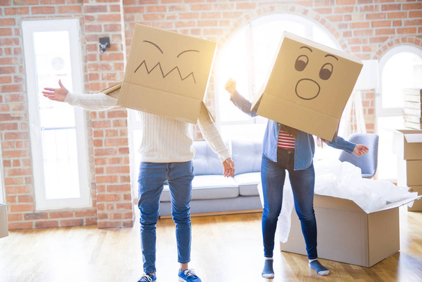 Verrücktes Paar trägt Schachteln mit lustigen Gesichtern über dem Kopf und freut sich über den Umzug in ein neues Haus - Foto, Bild