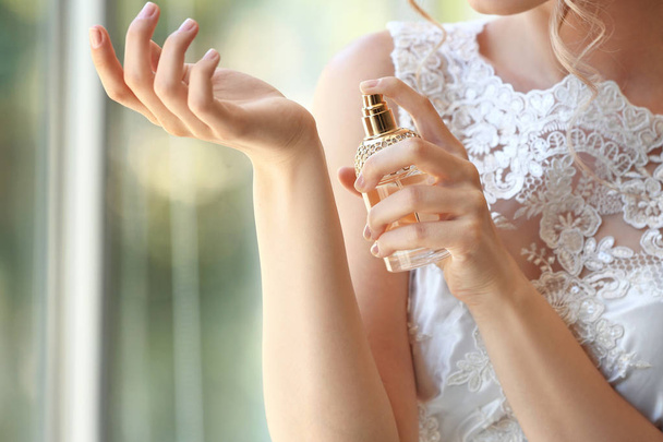 Beautiful young bride with bottle of perfume indoors, closeup - 写真・画像