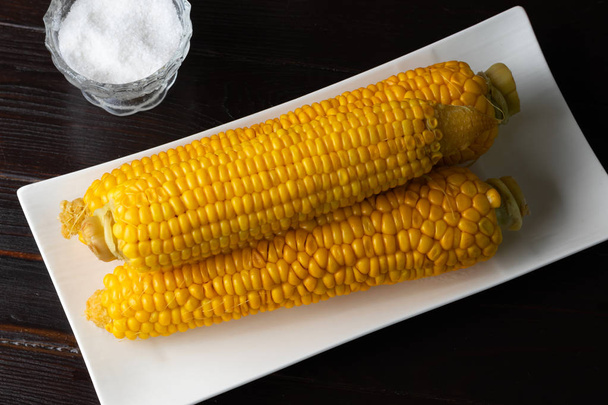 Gotowana kukurydza na białej płycie na ciemnym drewnianym stole. Zbliżenie - Zdjęcie, obraz