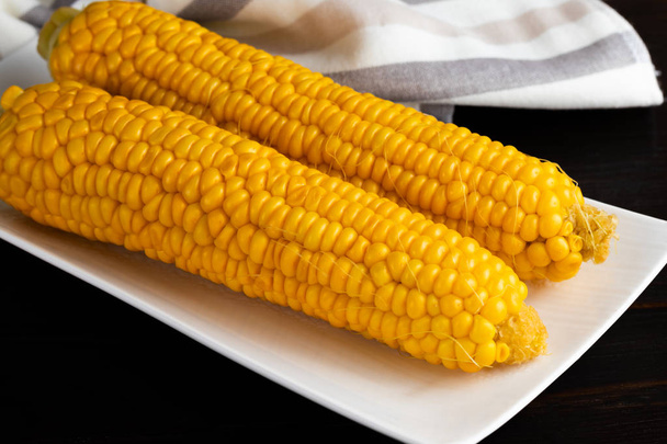 Gotowana kukurydza na białej płycie na ciemnym drewnianym stole. Zbliżenie - Zdjęcie, obraz