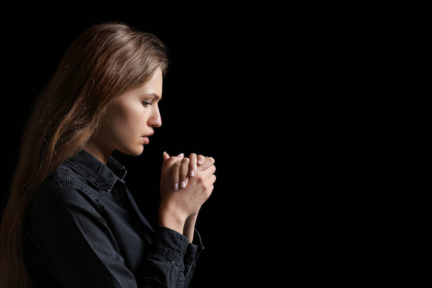 Dindar genç kadın karanlık arka planda Tanrı 'ya dua ediyor. - Fotoğraf, Görsel