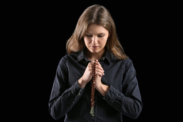 Θρησκευτική νεαρή γυναίκα προσεύχεται στο Θεό σε σκοτεινό φόντο - Φωτογραφία, εικόνα