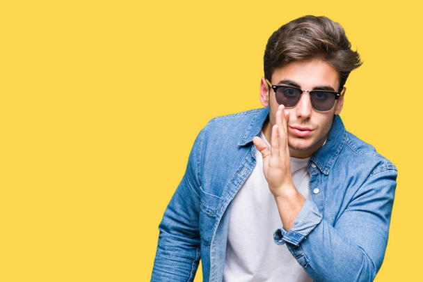 Young handsome man wearing sunglasses over isolated background hand on mouth telling secret rumor, whispering malicious talk conversation - Photo, Image