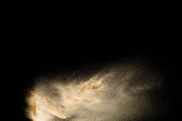 Brauner Sand plätschert vor dunklem Hintergrund. Trockener Flusssand Explosion isoliert auf schwarzem Hintergrund. abstrakte Sandwolke. - Foto, Bild