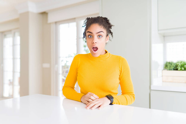 Hermosa mujer afroamericana con cabello afro vistiendo un suéter amarillo casual en la cara de choque, con aspecto escéptico y sarcástico, sorprendida con la boca abierta
 - Foto, imagen