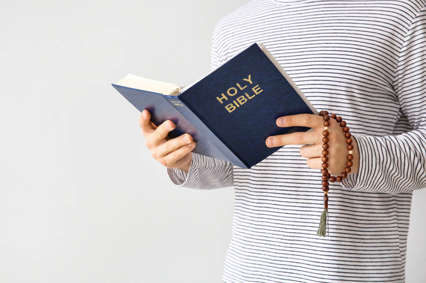 Religious young man reading Bible on light background - Photo, Image