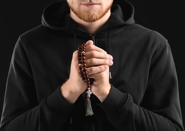Θρησκευόμενος νέος άνθρωπος προσεύχεται στο Θεό σε σκοτεινό φόντο, κοντινό πλάνο - Φωτογραφία, εικόνα