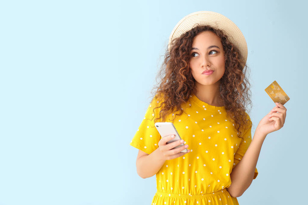 Femme afro-américaine réfléchie avec carte de crédit et téléphone mobile sur fond de couleur claire
 - Photo, image