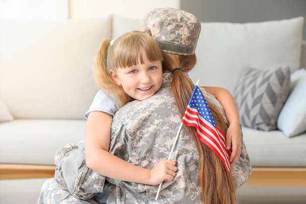 Happy female soldier of USA army hugging her little daughter at home - Фото, изображение
