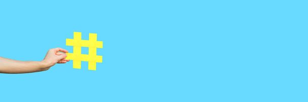 περικομμένη όψη του ανθρώπινου χεριού που δείχνει μεγάλο μεγάλο κίτρινο σύμβολο «#» σε γαλάζιο φόντο, σύμβολο μάρκετινγκ και έννοια των μέσων κοινωνικής δικτύωσης  - Φωτογραφία, εικόνα