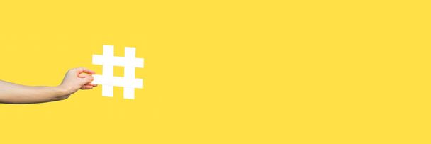 bijgesneden weergave van menselijke hand tonen grote grote witte hashtag teken op gele achtergrond, marketing symbool en sociale media concept  - Foto, afbeelding