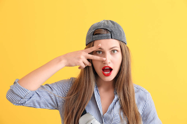 Stylish young woman showing victory gesture on color background - Foto, imagen