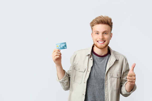 Joven feliz con tarjeta de crédito mostrando gesto de pulgar hacia arriba sobre fondo blanco
 - Foto, Imagen