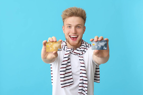 Happy young man with credit cards on color background - Foto, afbeelding
