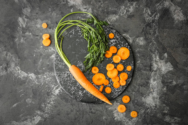 Board with fresh carrot and slices on dark background - Фото, изображение