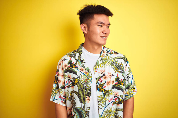 Asijský Číňan na prázdninách nosí letní košili přes izolované žluté pozadí a dívá se na stranu s úsměvem na tváři, přirozeným výrazem. Směje se sebevědomě. - Fotografie, Obrázek