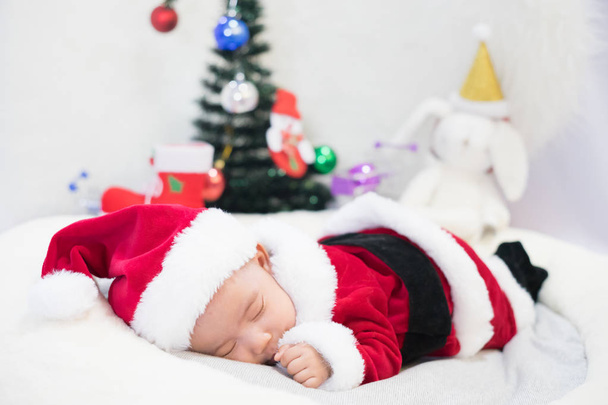 little baby wearing Santa Claus costume sleep on white fur carpet with Christmas tree. Concept of celebrates Christmas and New Year's holidays. - Foto, Imagen