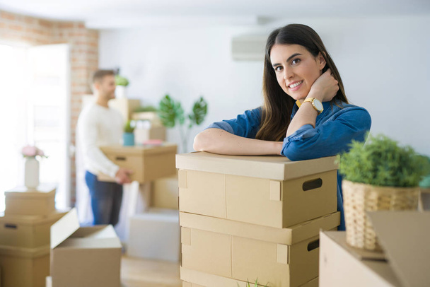 Young couple moving to a new home, beautiful woman smiling leaning on cardboard boxes - Foto, Imagem