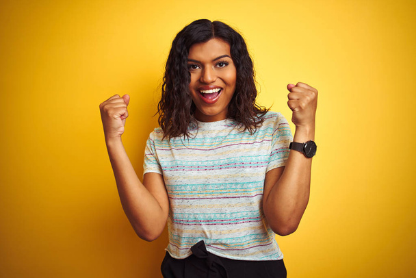 Beautiful transsexual transgender woman wearing t-shirt over isolated yellow background celebrating surprised and amazed for success with arms raised and open eyes. Winner concept. - Photo, Image