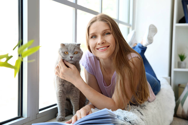 Piękna kobieta z cute kota w pobliżu okna w domu - Zdjęcie, obraz