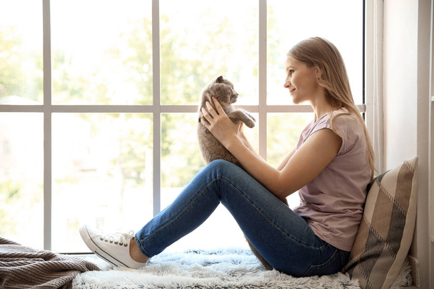Женщина с симпатичной кошкой, сидящей у окна
 - Фото, изображение