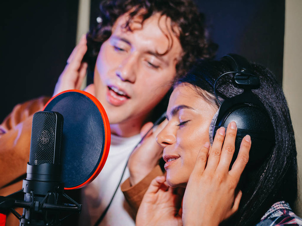 Young team of singers performing song in record studio.Professional musician duet recording new album.Beautiful couple working and singing near microphone together. - Foto, Imagem