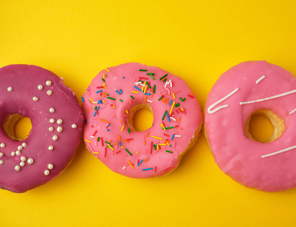 round different sweet donuts with sprinkles on a yellow backgrou - Fotoğraf, Görsel