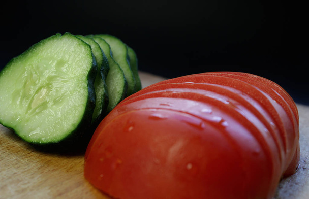 vastaviipaloitu kurkku ja tomaatti, puulaudalla mustalla pohjalla
 - Valokuva, kuva