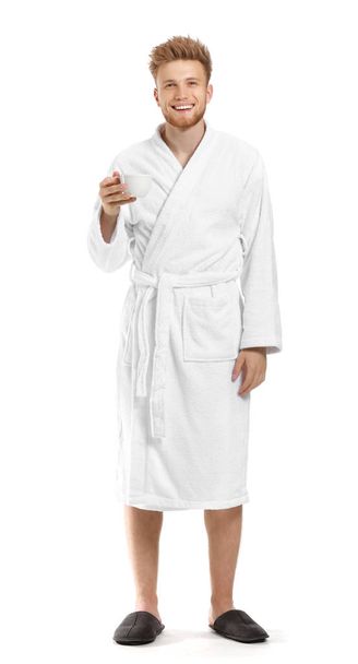 Handsome young man in bathrobe drinking coffee on white background - 写真・画像