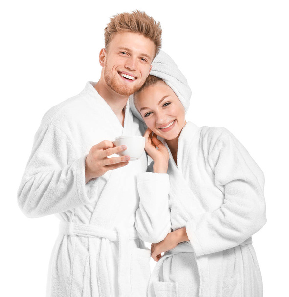 Feliz pareja joven en albornoces y con taza de café sobre fondo blanco
 - Foto, Imagen